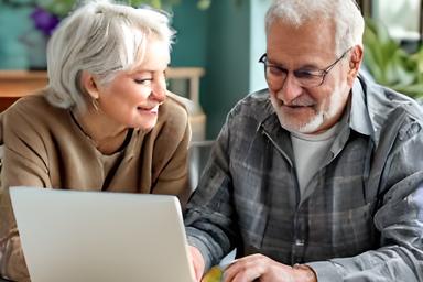 Twee senioren zitten samen achter een laptop tijdens een basis computercursus in Tilburg, wijzend naar het scherm